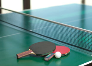 Two table tennis or ping pong rackets and balls on a green table with net
